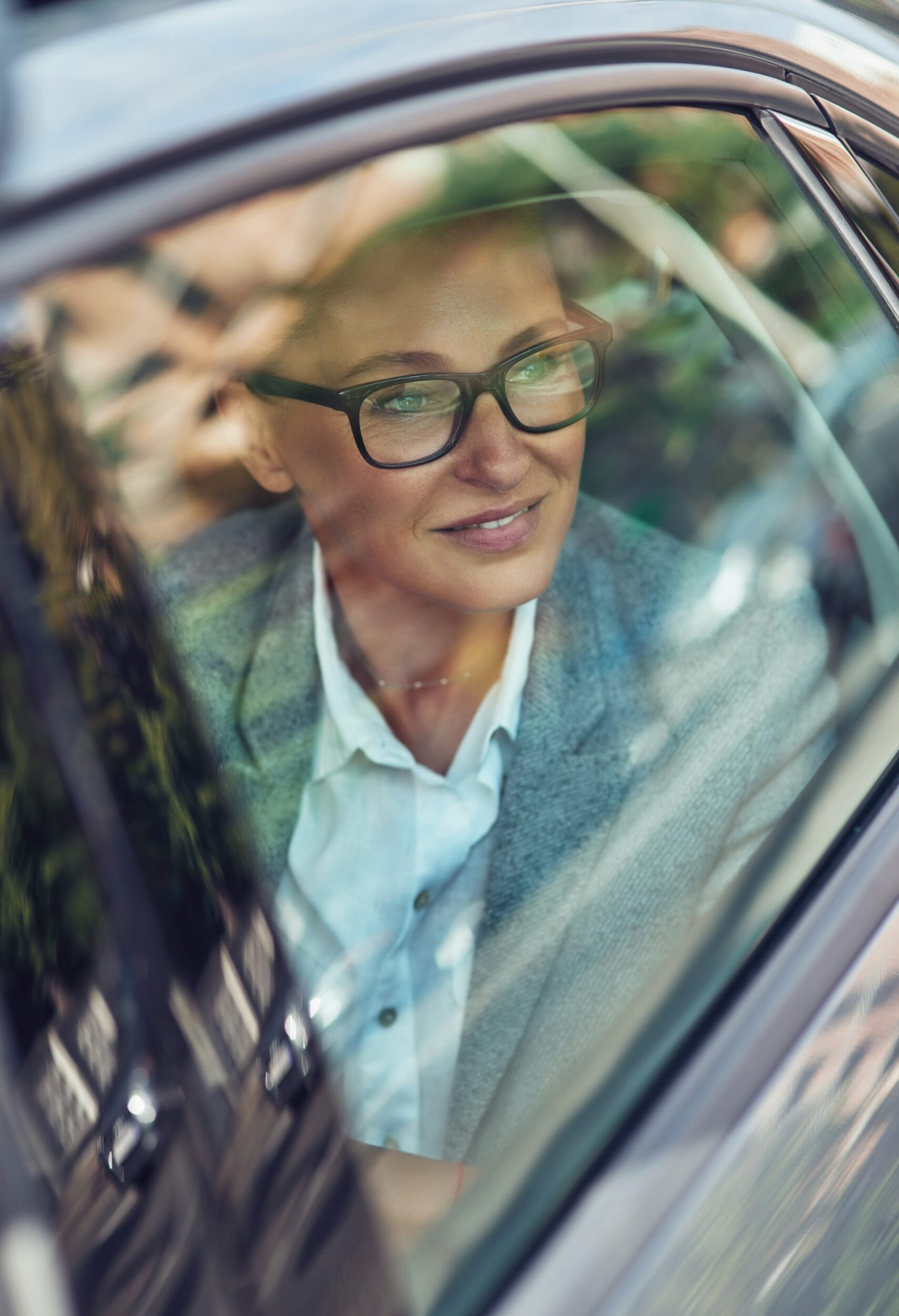 Transportation and vehicle concept, beautiful and happy middle aged business woman wearing eyeglasses looking out of a car window and smiling, sitting on back seat in taxi, business trip